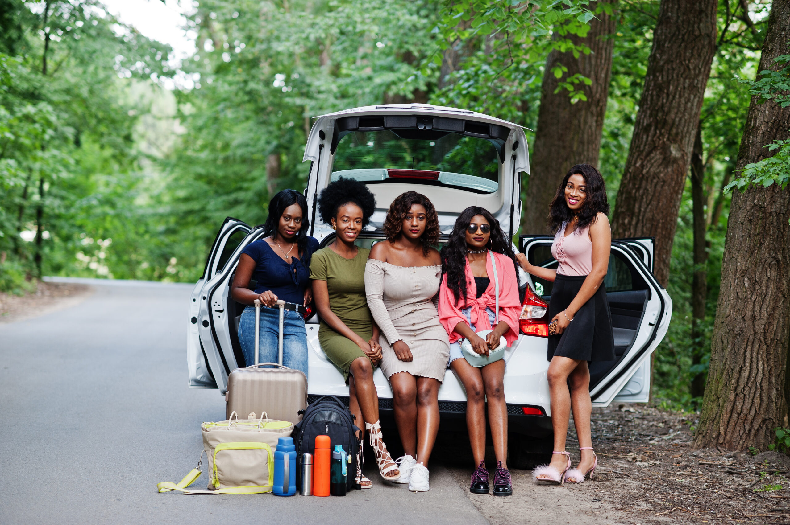 groupe de cinq joyeuses voyageuses afro americaines assises dans le coffre ouvert de la voiture scaled